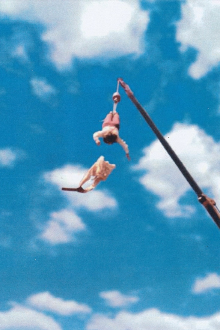Troy Milligan in a straitjacket, hanging upside down from a crane
